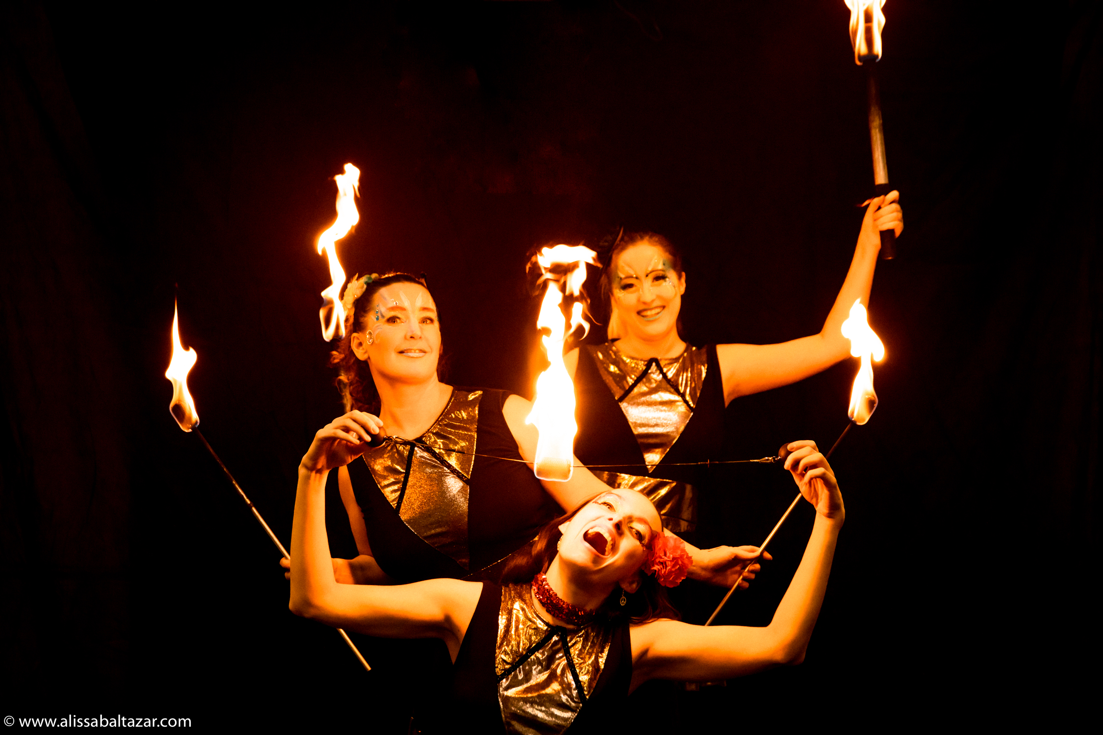 Fire dancers posing in a trio with fire torches and a fire orb from Hoop You