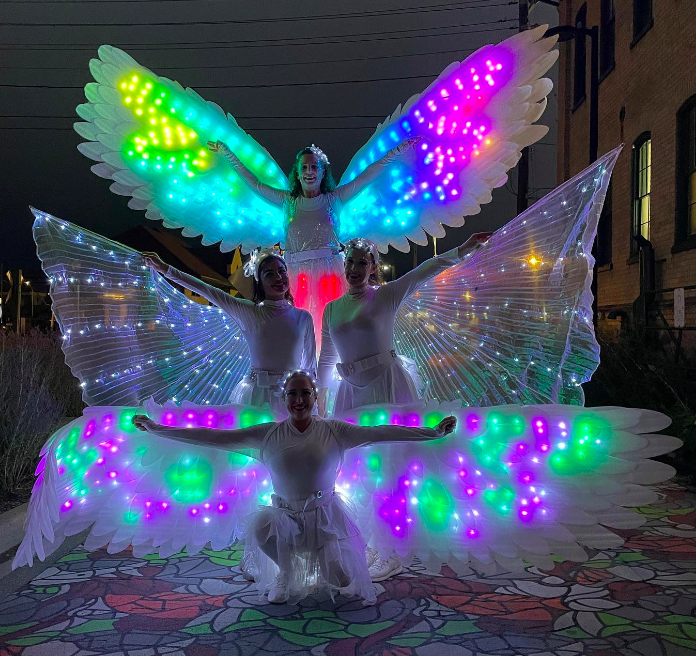 glow isis wings and glow angle wings lit up in multiple colours with girls in white costumes arms outstretched