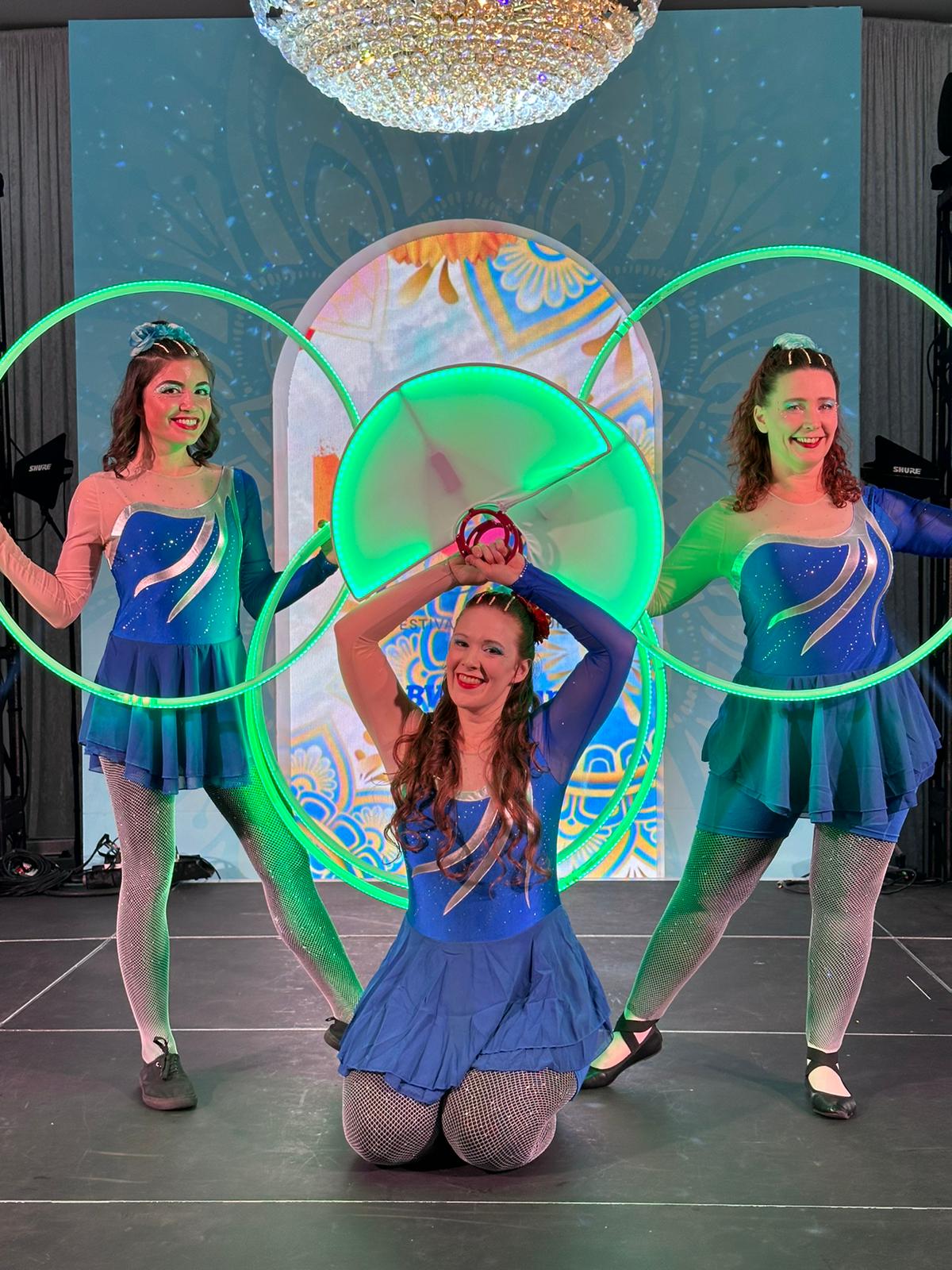led glow show, a trio of women pose in blue and silver dresses with green glowing led hula hoops and led moon fans 